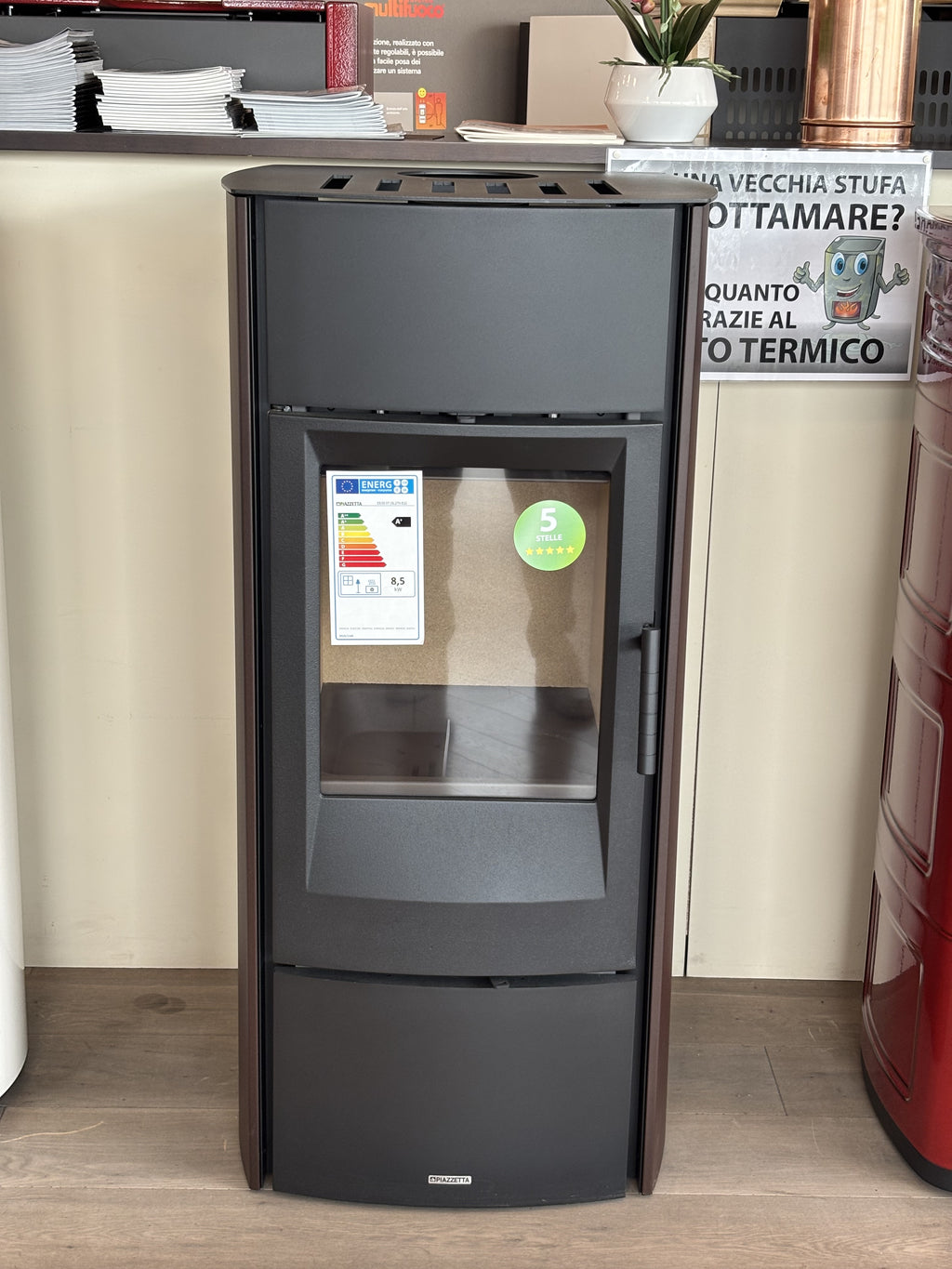 Stufa a legna Piazzetta E 530 Steel con design moderno e rivestimento in acciaio, visibile con porta e maniglie.