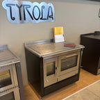 Stufa a legna Tyrola TR C 80 in acciaio nero, con porta in vetro e maniglie in legno, ideale per riscaldare ambienti domestici.